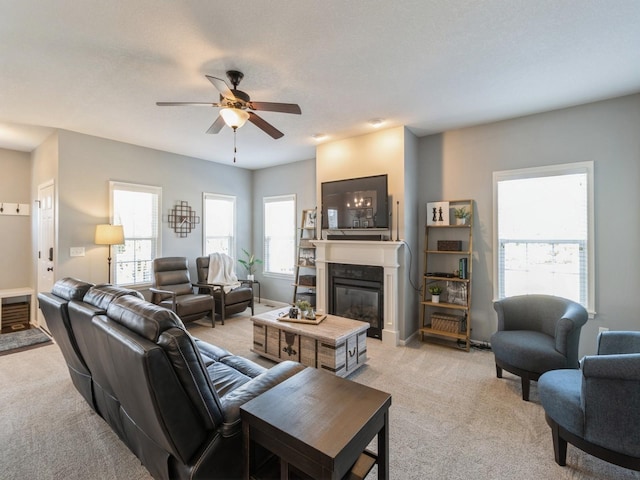 living room with light carpet, a glass covered fireplace, baseboards, and a ceiling fan