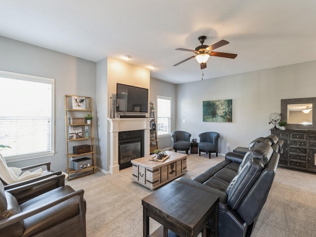 living area featuring baseboards, light carpet, a glass covered fireplace, and a ceiling fan