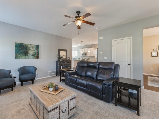 living area featuring light carpet, visible vents, baseboards, and a ceiling fan