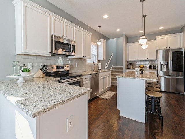 kitchen with a peninsula, white cabinets, dark wood-style floors, and stainless steel appliances