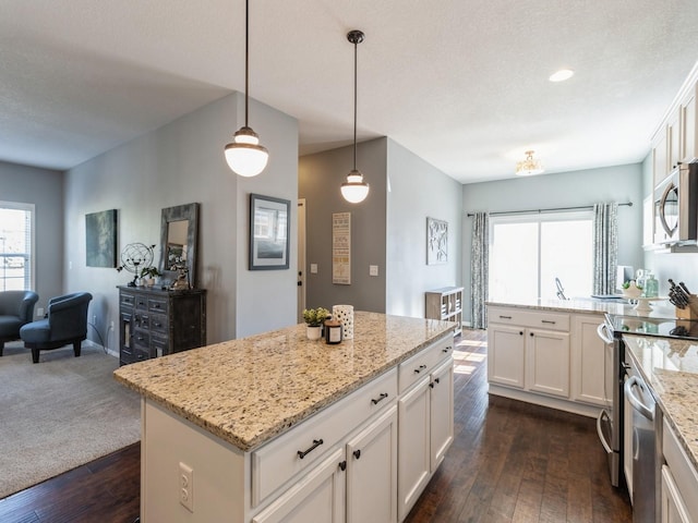 kitchen with dark wood finished floors, open floor plan, light stone counters, stainless steel appliances, and white cabinetry