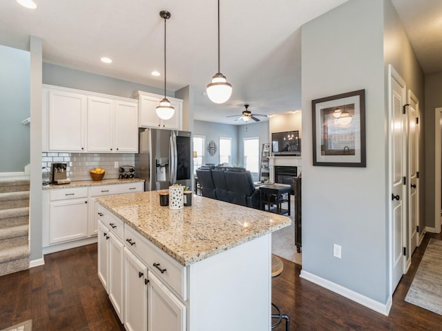 kitchen featuring ceiling fan, white cabinets, stainless steel refrigerator with ice dispenser, backsplash, and a center island