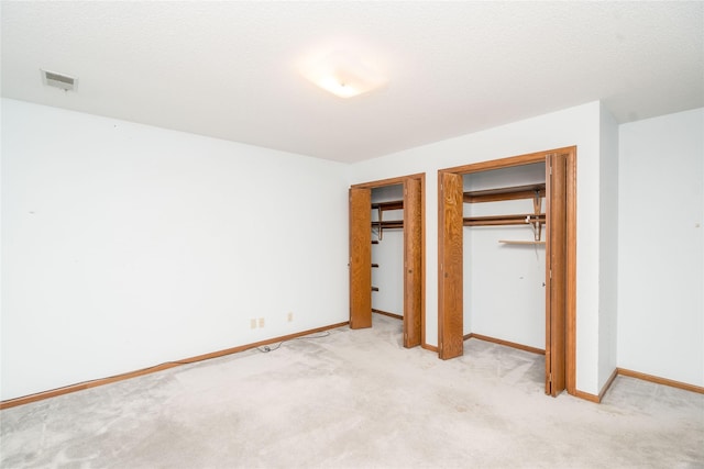 unfurnished bedroom featuring visible vents, multiple closets, a textured ceiling, baseboards, and light colored carpet