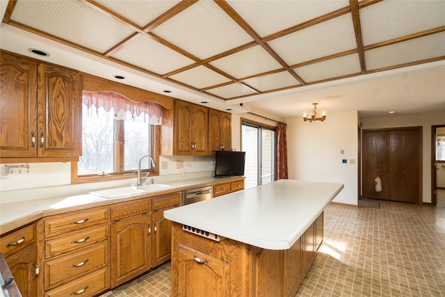 kitchen with an inviting chandelier, a sink, light countertops, brown cabinets, and a center island