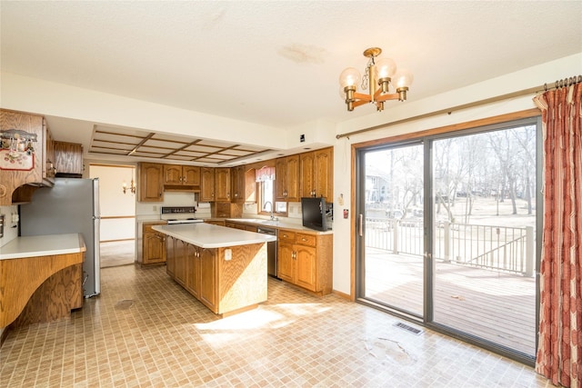 kitchen featuring brown cabinets, a notable chandelier, a kitchen island, appliances with stainless steel finishes, and light countertops