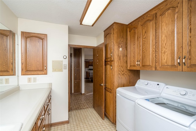 washroom with a textured ceiling, cabinet space, and washer and clothes dryer