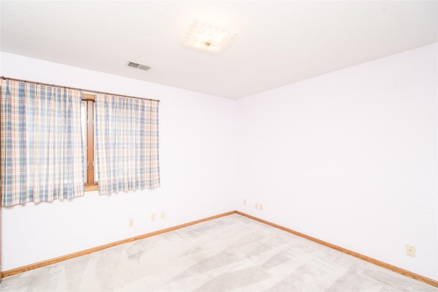 spare room featuring light colored carpet, visible vents, and baseboards