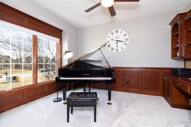 living area with a ceiling fan, a wainscoted wall, and light carpet