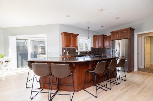 kitchen featuring light wood-type flooring, decorative backsplash, stainless steel fridge, and a center island