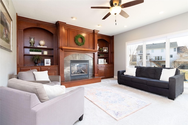 living area with light carpet, built in features, a fireplace, and ceiling fan