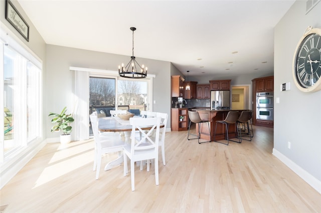 dining area with visible vents, light wood-style flooring, baseboards, and an inviting chandelier