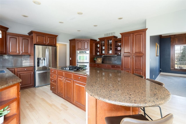 kitchen featuring visible vents, a center island, light stone counters, appliances with stainless steel finishes, and a kitchen breakfast bar