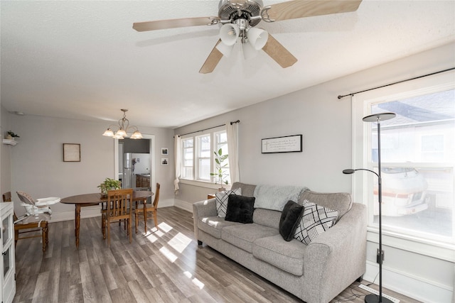 living area featuring baseboards, wood finished floors, and ceiling fan with notable chandelier