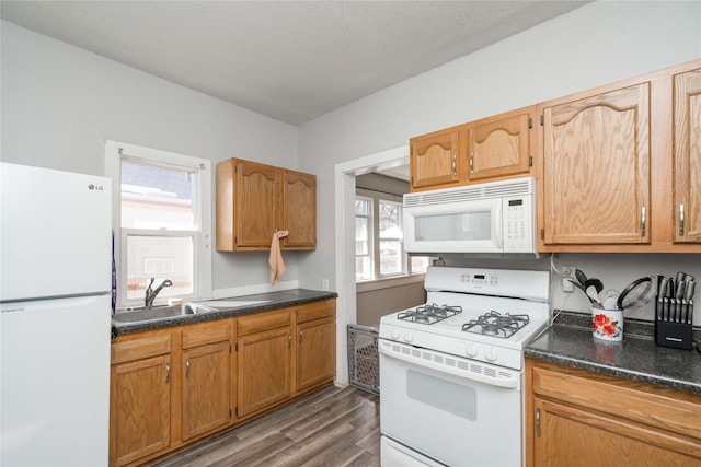 kitchen featuring light wood-type flooring, a sink, dark countertops, a textured ceiling, and white appliances