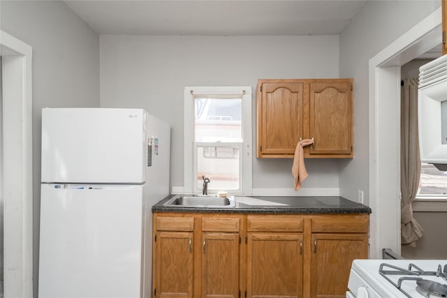 kitchen featuring white appliances, dark countertops, and a sink