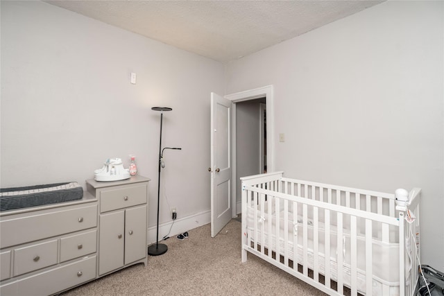 bedroom featuring a textured ceiling, a crib, baseboards, and light carpet