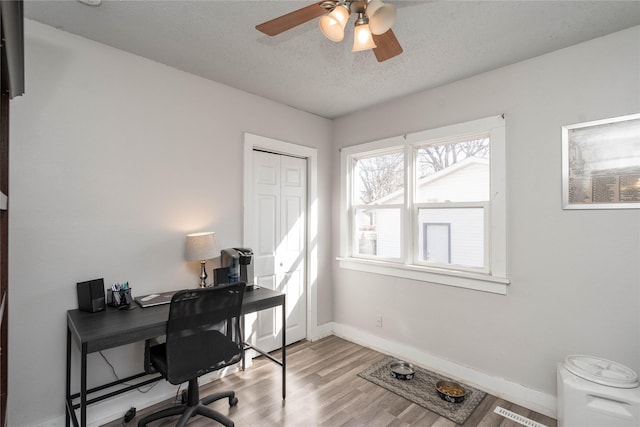 office featuring visible vents, baseboards, ceiling fan, light wood-style floors, and a textured ceiling