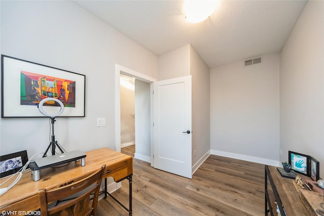 office featuring visible vents, a textured ceiling, baseboards, and light wood-style floors