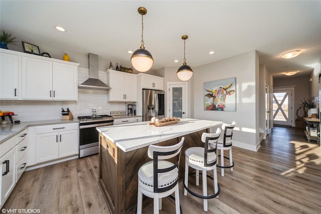 kitchen with wall chimney range hood, a kitchen island, stainless steel appliances, a kitchen breakfast bar, and tasteful backsplash