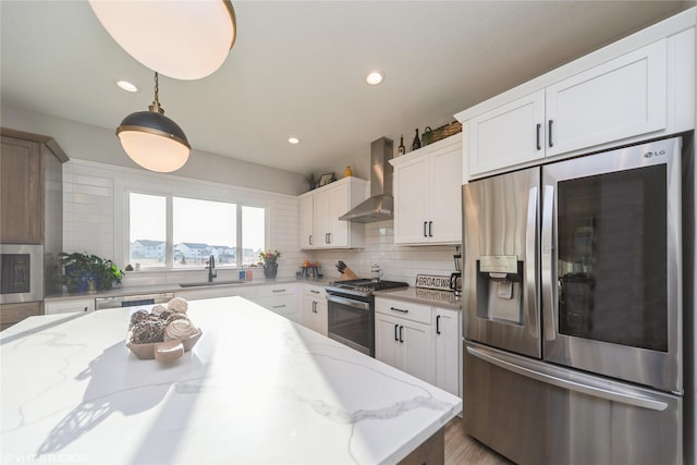 kitchen featuring a sink, stainless steel appliances, white cabinets, wall chimney range hood, and tasteful backsplash