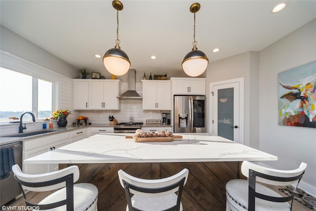 kitchen featuring a kitchen island, a sink, stainless steel appliances, wall chimney exhaust hood, and tasteful backsplash