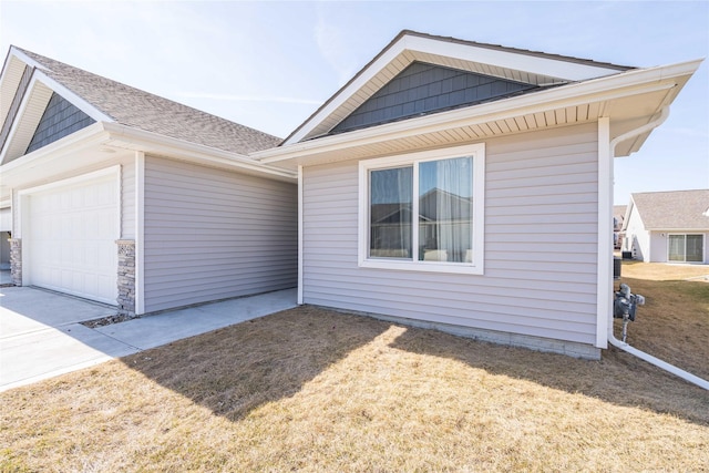 view of side of property with an attached garage, driveway, and roof with shingles