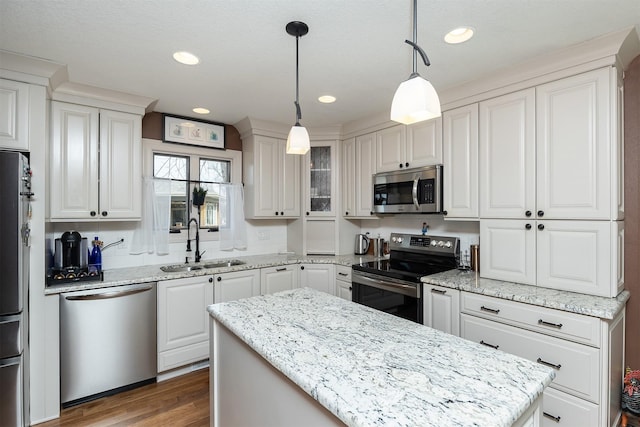 kitchen with a sink, wood finished floors, recessed lighting, appliances with stainless steel finishes, and hanging light fixtures