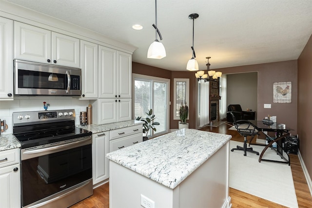 kitchen with a kitchen island, light stone countertops, light wood-style flooring, an inviting chandelier, and stainless steel appliances