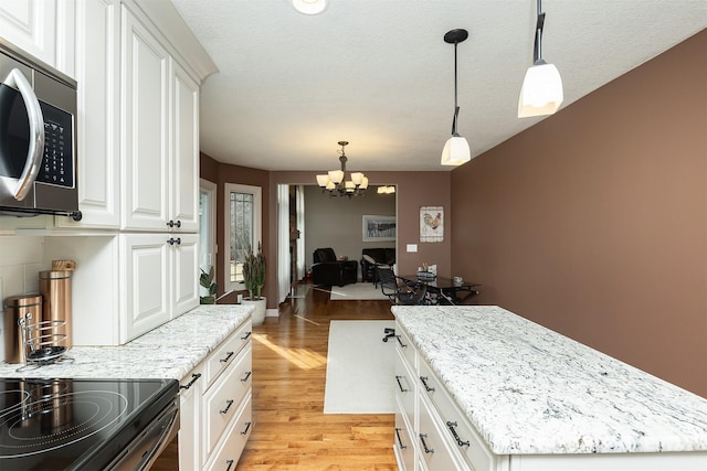 kitchen with stainless steel microwave, light wood-type flooring, light stone counters, a notable chandelier, and white cabinets