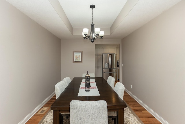 dining area with a tray ceiling, wood finished floors, baseboards, and a chandelier