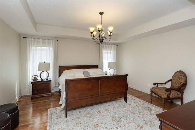 bedroom featuring baseboards, a raised ceiling, an inviting chandelier, and wood finished floors