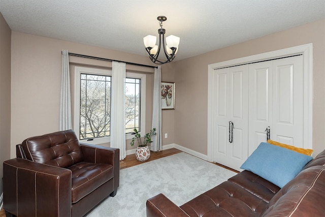 living area featuring a notable chandelier, a textured ceiling, baseboards, and wood finished floors