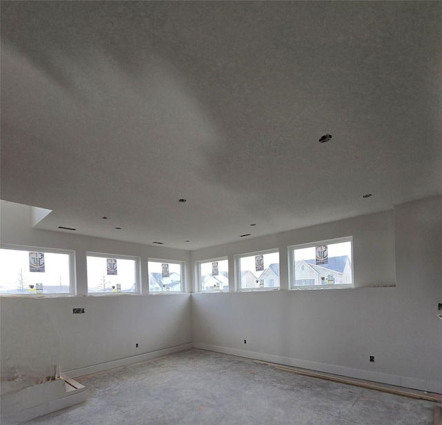 unfurnished room with plenty of natural light, baseboards, and concrete floors