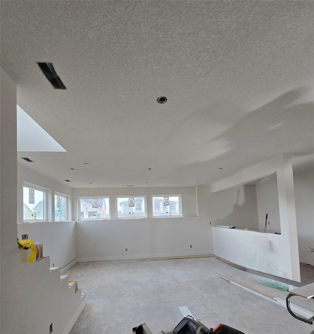 unfurnished room with baseboards, a textured ceiling, and a healthy amount of sunlight