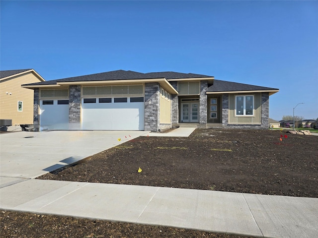 prairie-style home featuring a garage, central air condition unit, stone siding, and concrete driveway