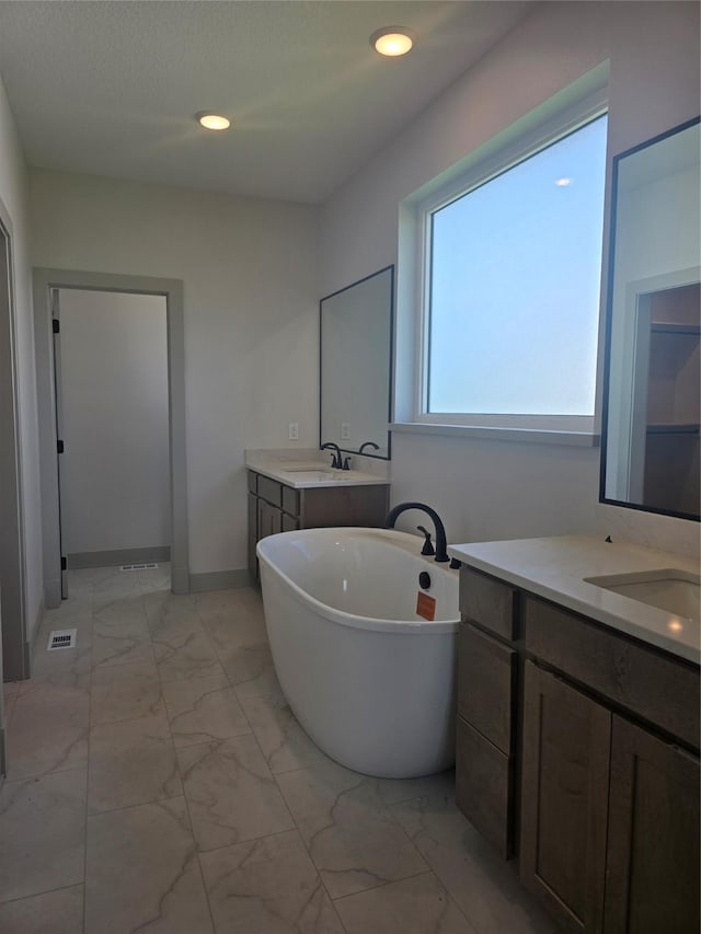 16203 Goodman Dr, Urbandale, IA 50323 - full bath with marble look tile flooring, a freestanding tub, two vanities, and recessed lighting