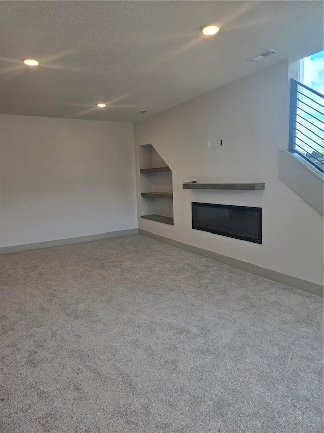 16203 Goodman Dr, Urbandale, IA 50323 - unfurnished living room with carpet flooring, built in features, a textured ceiling, a glass covered fireplace, and recessed lighting