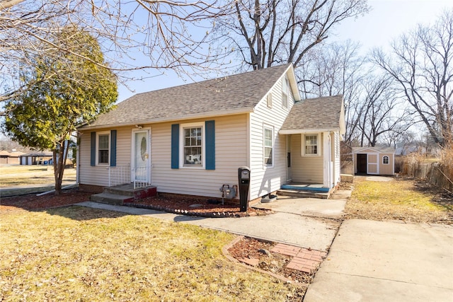 bungalow with a storage unit, roof with shingles, an outdoor structure, and a front lawn