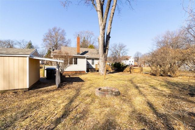 view of yard with a carport, a fire pit, an outdoor structure, and fence