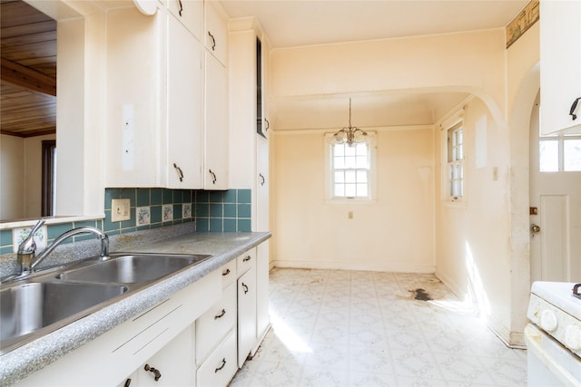 kitchen featuring a sink, tasteful backsplash, arched walkways, white cabinets, and light floors