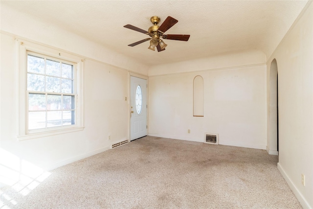 carpeted empty room with a textured ceiling, arched walkways, visible vents, and ceiling fan