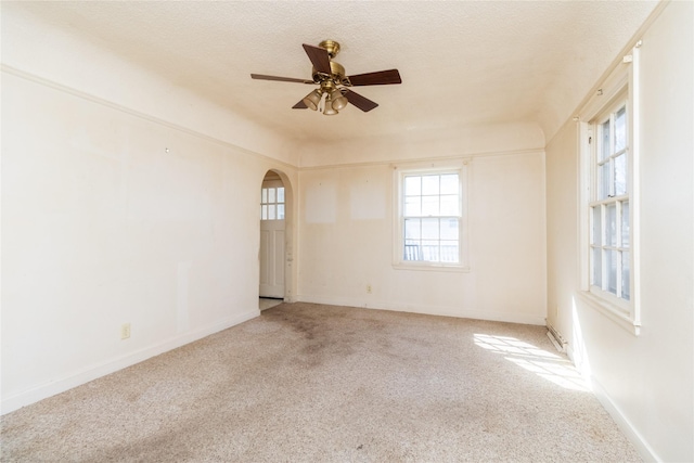 unfurnished room with a textured ceiling, carpet floors, arched walkways, baseboards, and ceiling fan