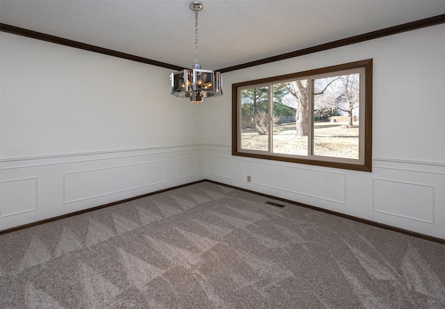 spare room with visible vents, ornamental molding, a textured ceiling, an inviting chandelier, and dark colored carpet