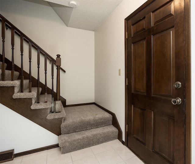 stairway featuring tile patterned floors, baseboards, visible vents, and a textured ceiling