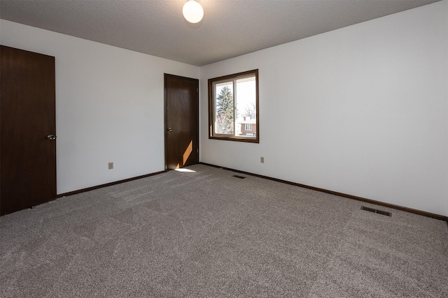 empty room with carpet flooring, a textured ceiling, baseboards, and visible vents