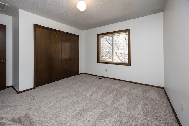 unfurnished bedroom featuring baseboards, visible vents, a closet, a textured ceiling, and light carpet