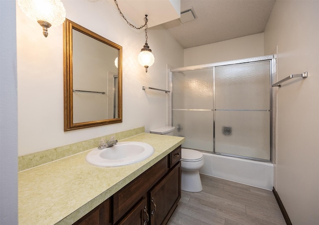 bathroom with visible vents, toilet, wood finished floors, enclosed tub / shower combo, and vanity