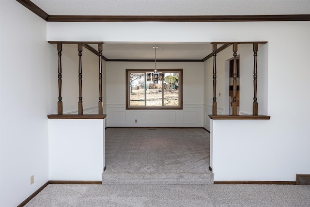 unfurnished dining area with a wainscoted wall, an inviting chandelier, crown molding, and carpet