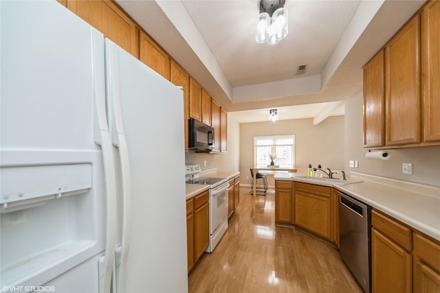 kitchen featuring white appliances, light countertops, light wood-type flooring, and a sink