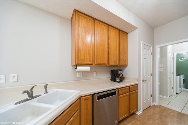 kitchen with a sink, a textured ceiling, light countertops, washer / dryer, and dishwasher